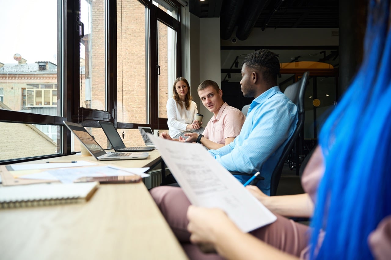 team of people sat around a desk with laptops and paperwork